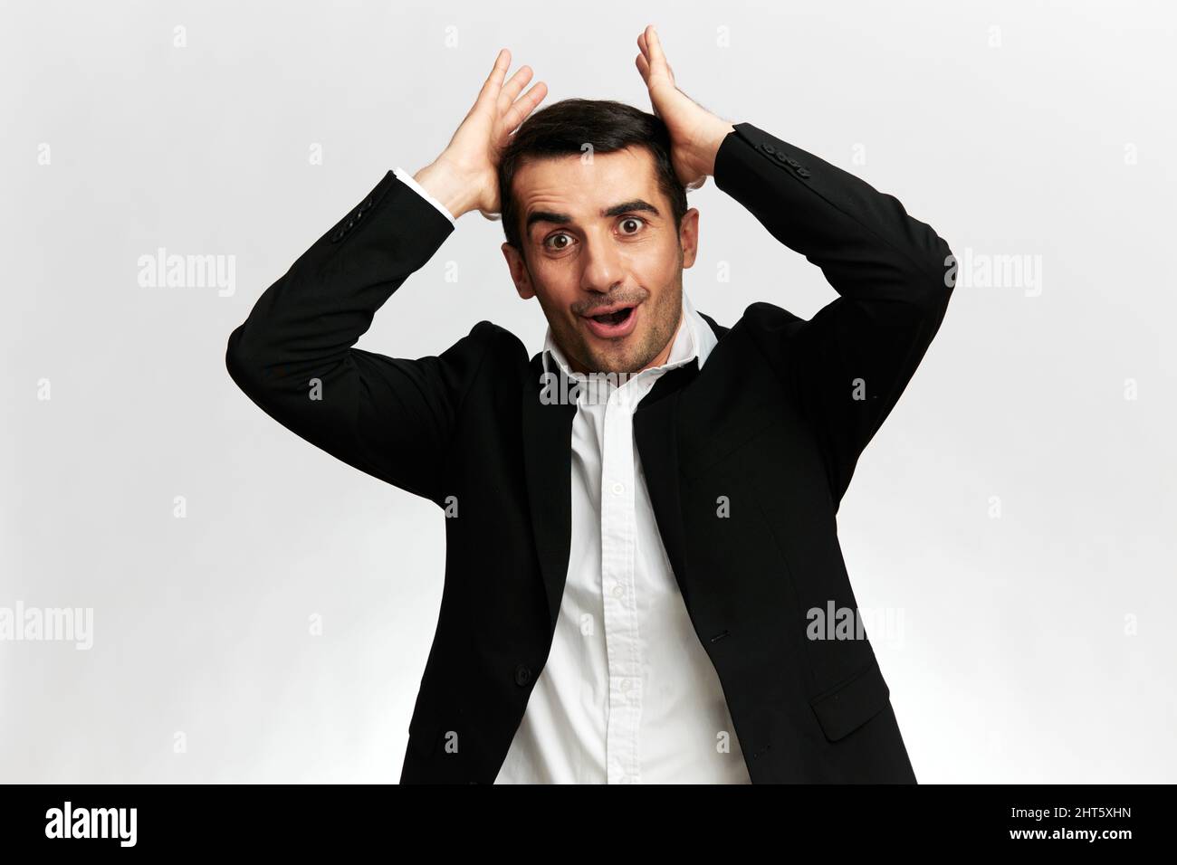 ritratti di un uomo in un abito nero da lavoro con un'espressione sorpresa raddrizza i capelli su uno sfondo bianco studio, copia spazio Foto Stock