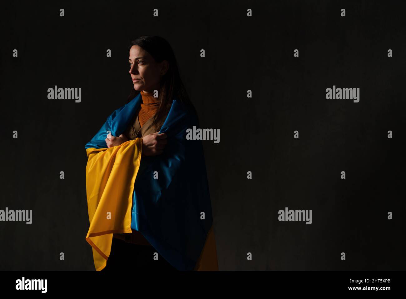 Donna triste coperta di bandiera Ucraina. Concetto di stare con la nazione Ucraina in guerra con la Russia. Foto Stock