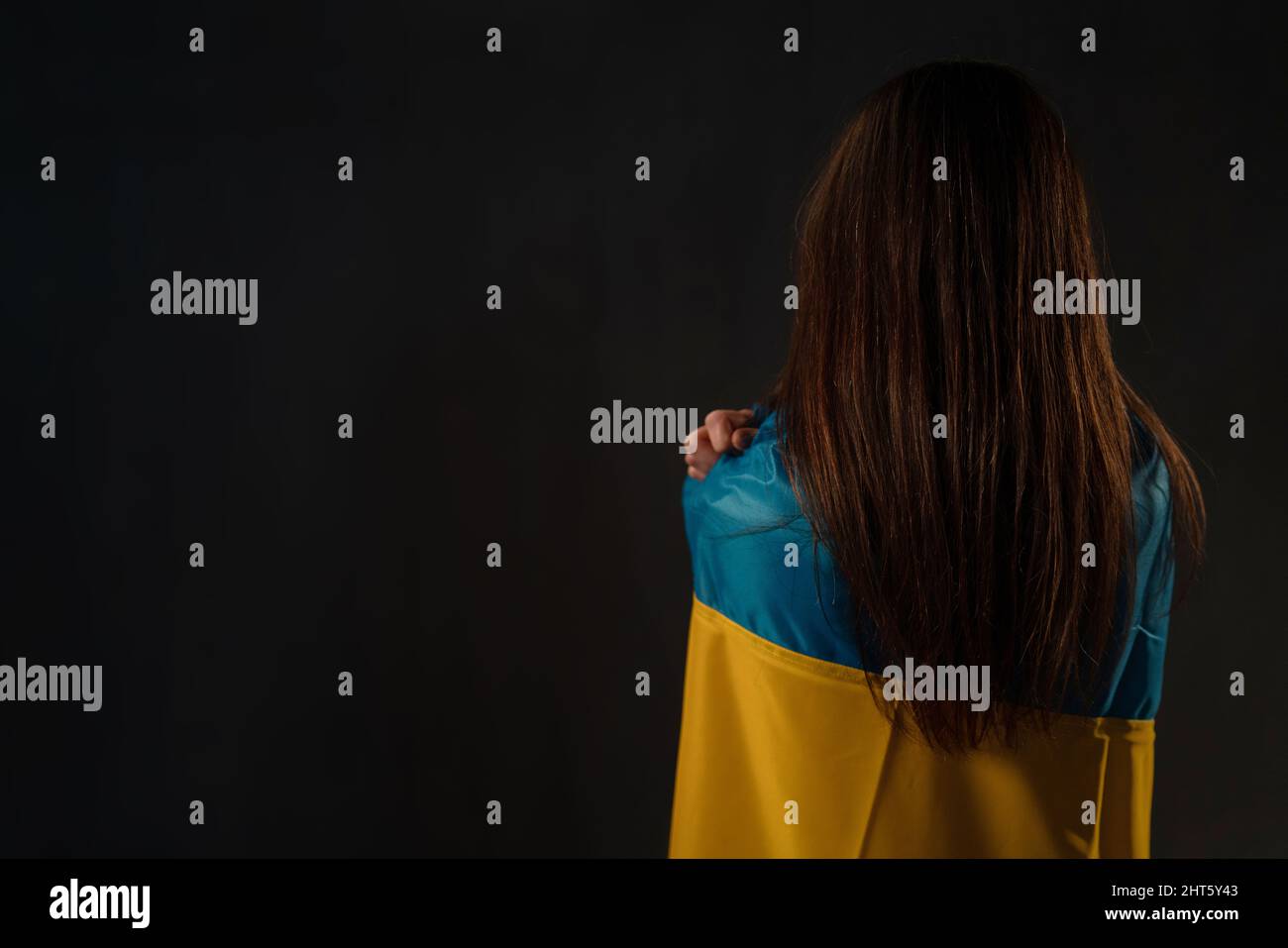 Vista posteriore della donna coperta dalla bandiera Ucraina. Concetto di stare con la nazione Ucraina in guerra con la Russia. Foto Stock