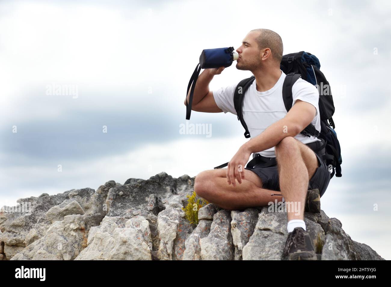 Percorrere la strada meno percorsa. Un giovane uomo che fa una pausa dalle escursioni mentre si siede su una roccia e beve un po' d'acqua. Foto Stock