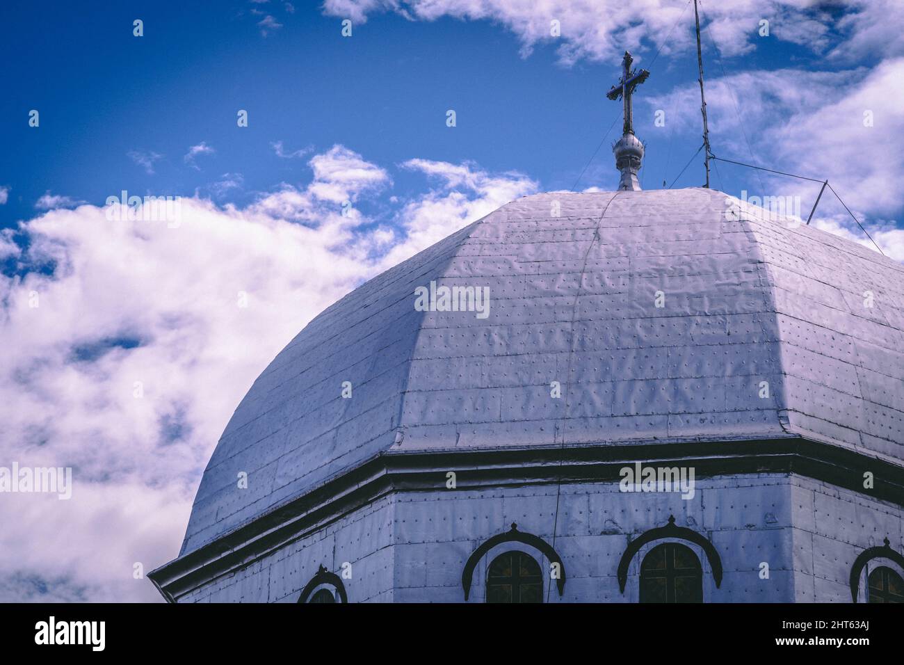 Un primo colpo del tetto esterno rotondo della chiesa con la croce e il cielo nuvoloso sullo sfondo Foto Stock