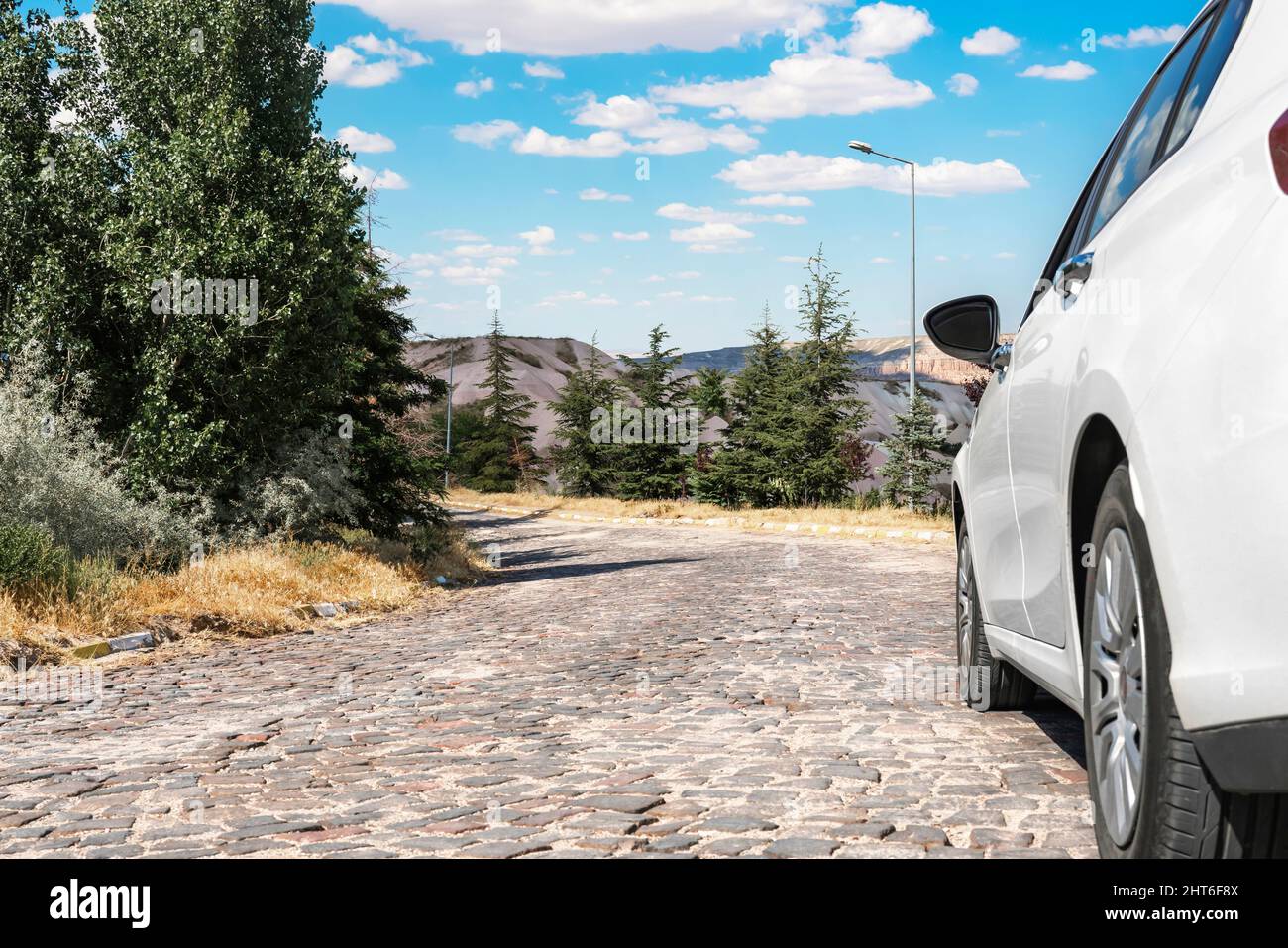 L'auto bianca si trova su una strada di montagna con una superficie di pietra sullo sfondo di montagne e foreste. Foto Stock