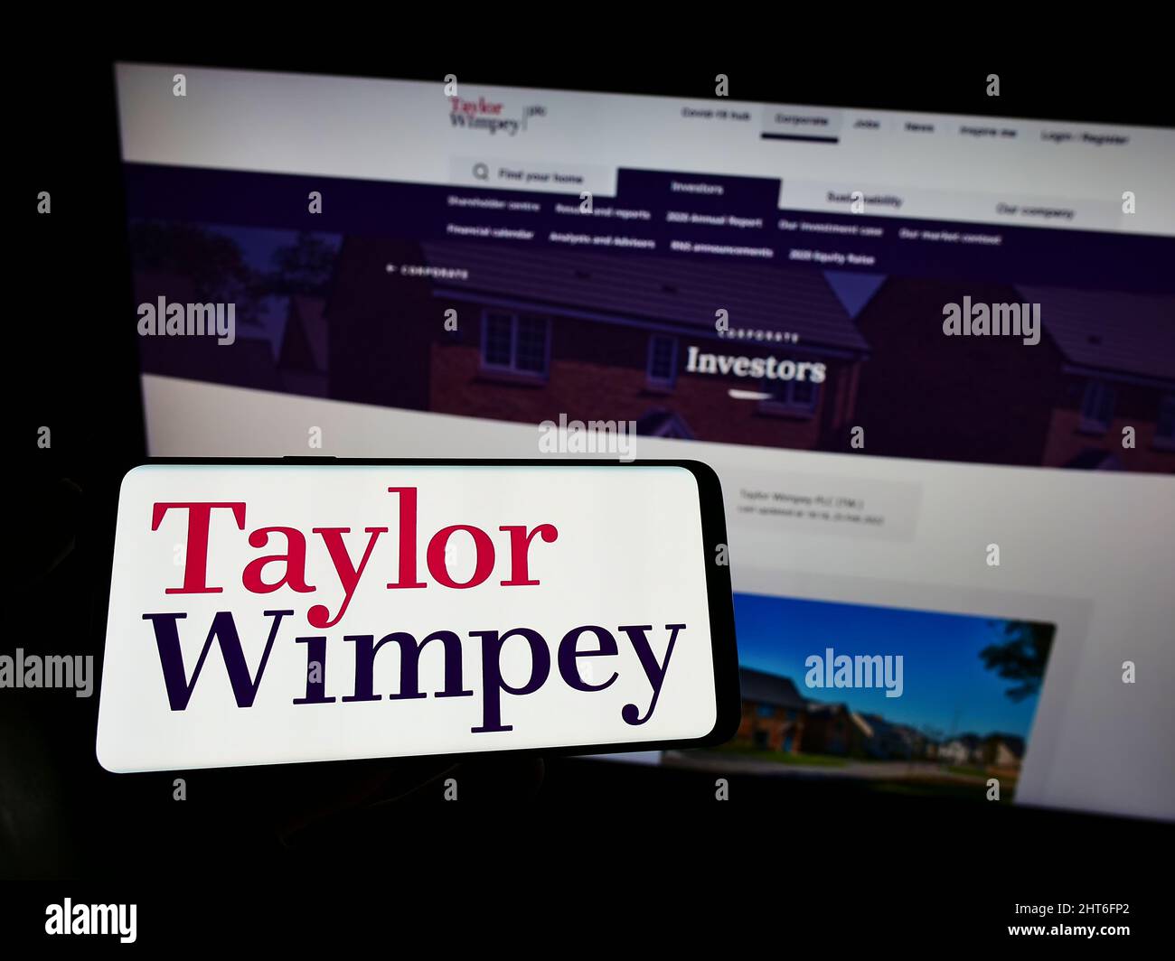 Persona che tiene il cellulare con il logo della casa britannica Taylor Wimpey plc sullo schermo di fronte al sito web. Mettere a fuoco sul display del telefono. Foto Stock