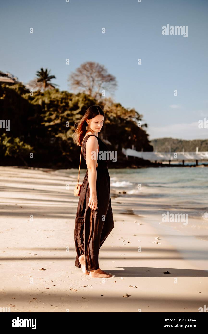 Scatto a corpo pieno di una giovane donna tedesca che indossa un abito estivo nero su una spiaggia sabbiosa in Thailandia Foto Stock