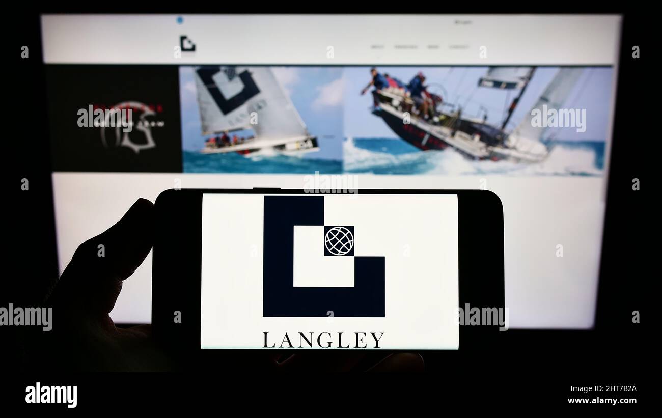 Persona che tiene uno smartphone con il logo della società di ingegneria britannica Langley Holdings plc sullo schermo di fronte al sito web. Mettere a fuoco sul display del telefono. Foto Stock