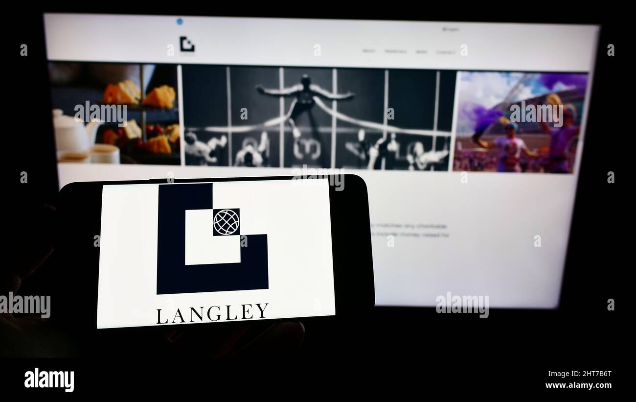 Persona che tiene il cellulare con il logo della società di ingegneria britannica Langley Holdings plc sullo schermo di fronte al sito web. Mettere a fuoco sul display del telefono. Foto Stock