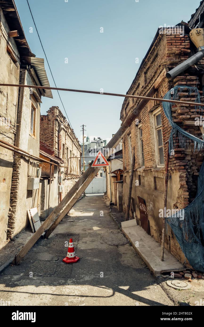 Vecchi edifici in crolli con supporti in legno e segnaletica stradale di avvertimento a Tbilisi, Georgia. Foto Stock