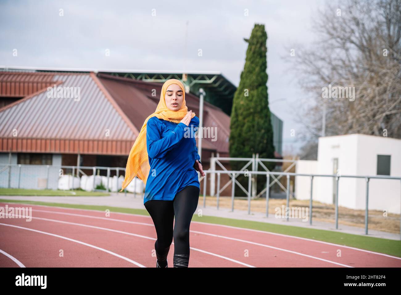 Sportivo etnico attivo in hijab che corre su pista Foto Stock