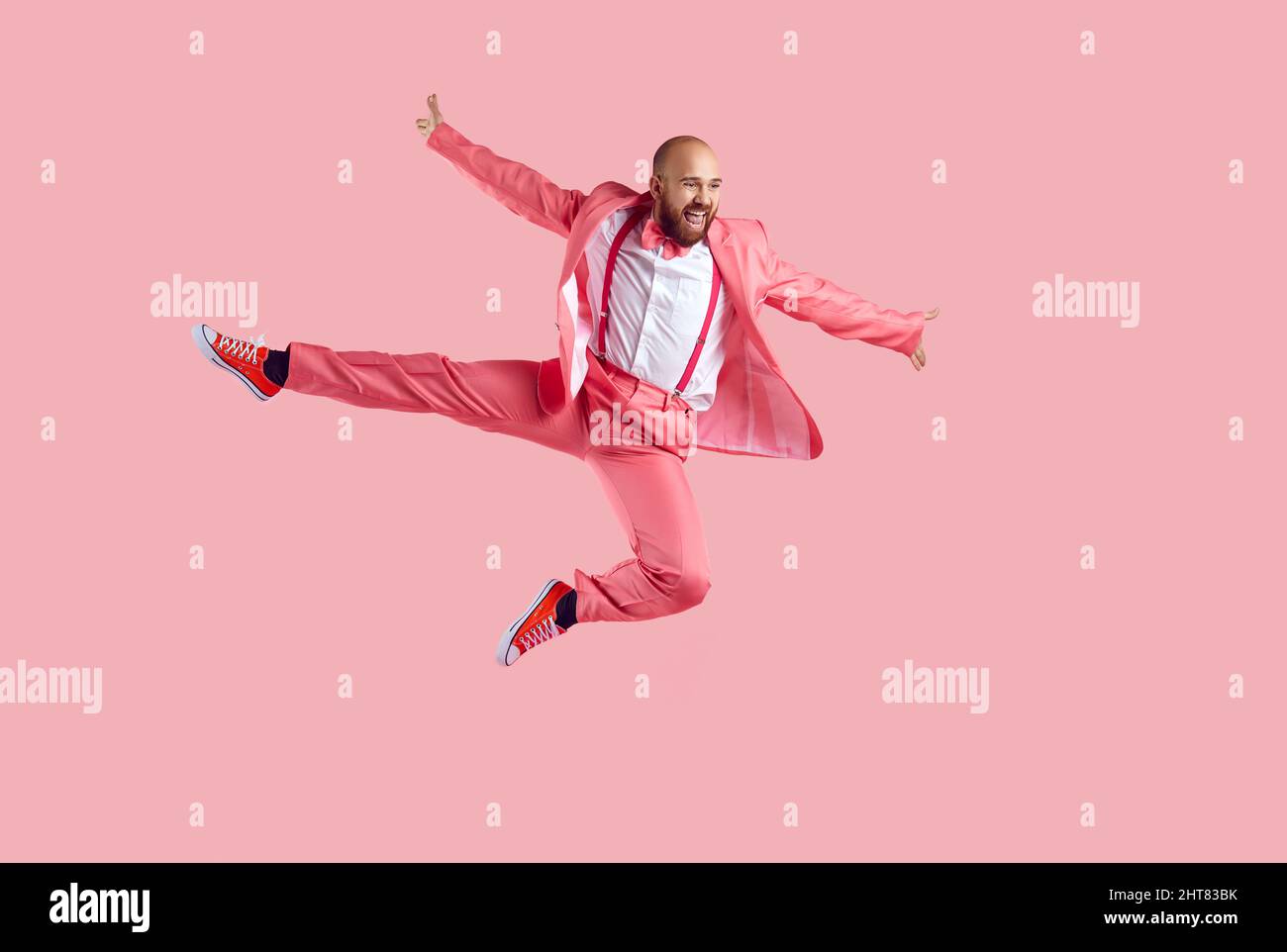 Felice divertente giovane ballerino maschile che salta in alto in aria isolato su uno sfondo rosa Foto Stock