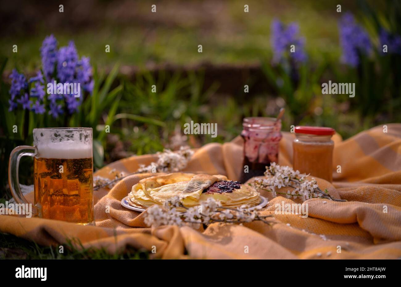 Un primo piano di tazze di birra durante un picnic un piatto di pancake con marmellata sull'erba Foto Stock