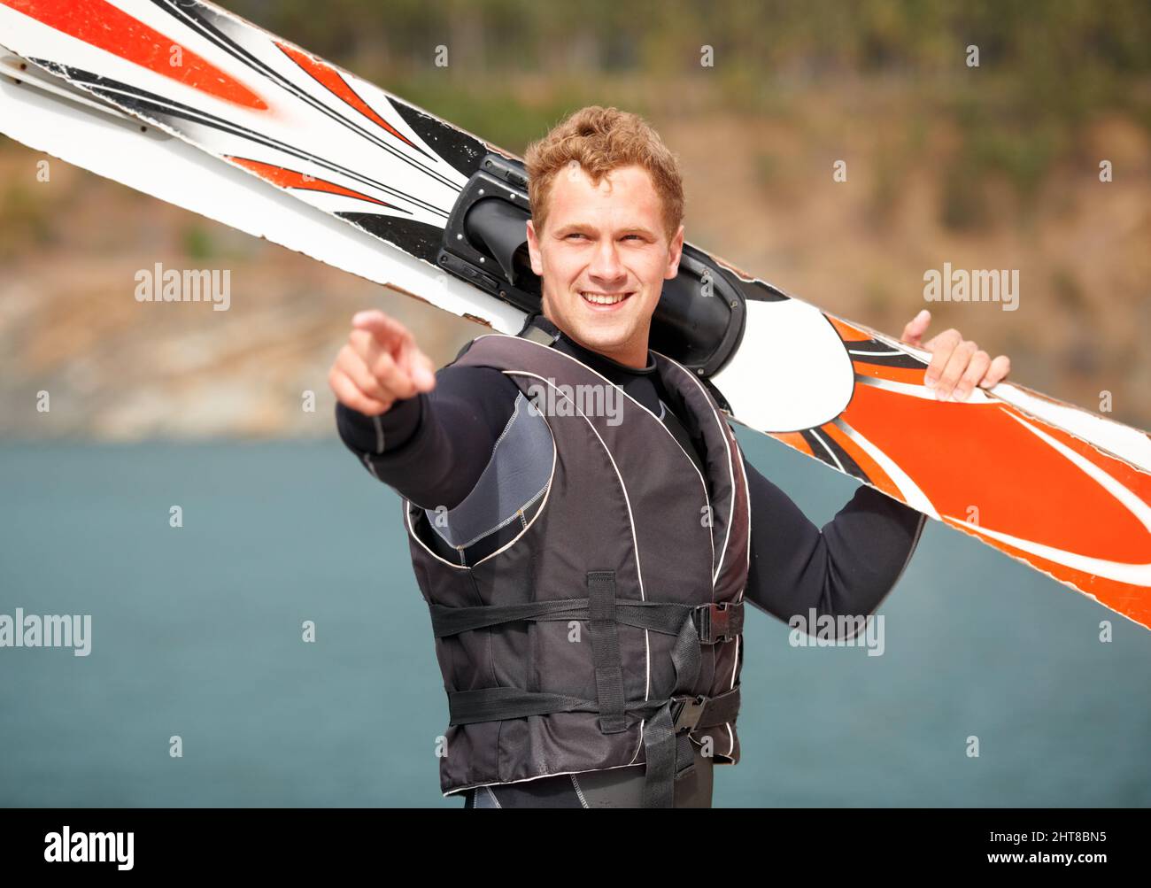 Guardate quel ragazzo lì. Sorridendo sciatore d'acqua che tiene i suoi sci lungo il lago e punta. Foto Stock