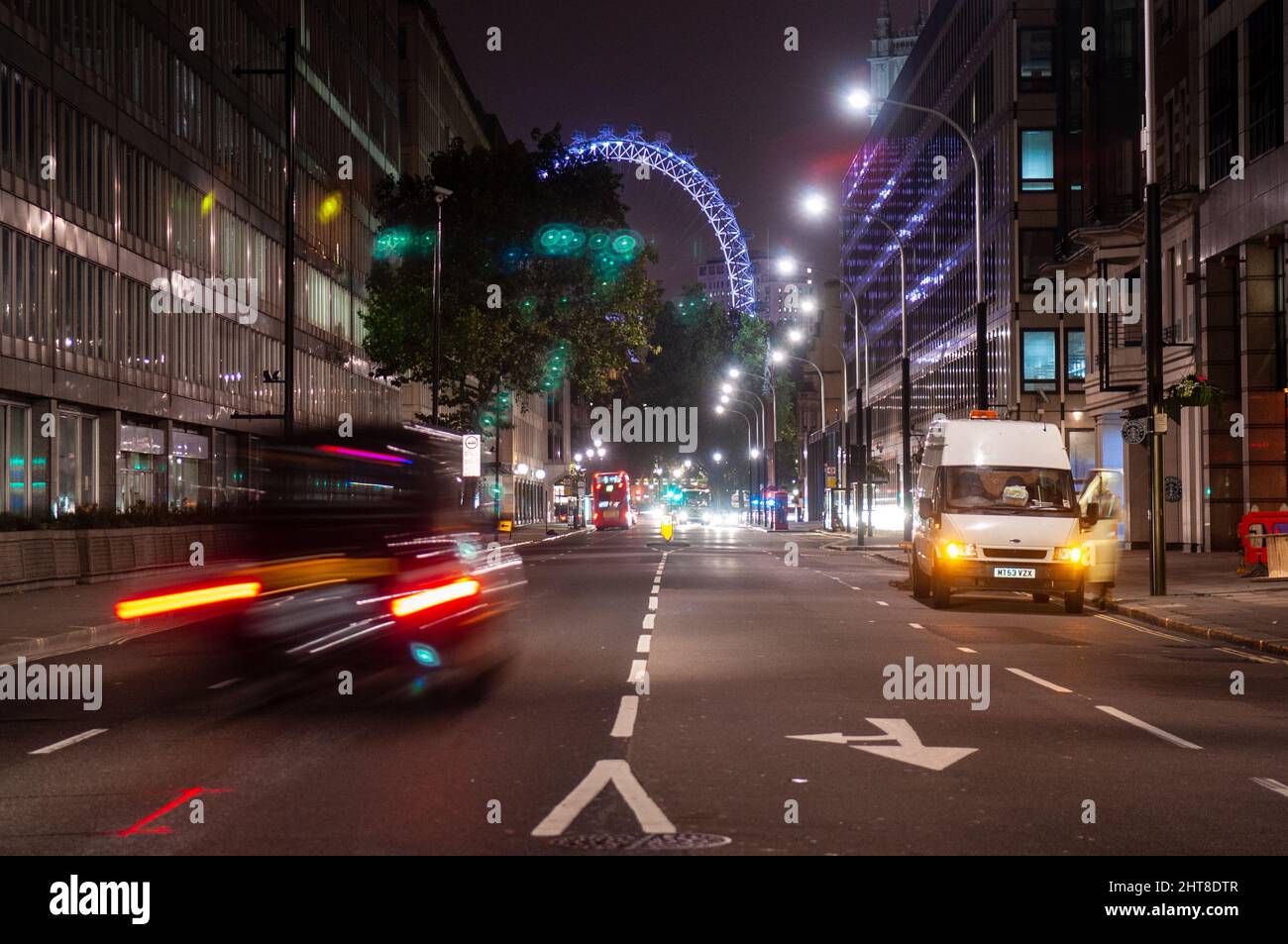 Il traffico scorre di notte tra gli edifici di uffici in Victoria Street di Westminster, con il London Eye illuminato in lontananza. Foto Stock