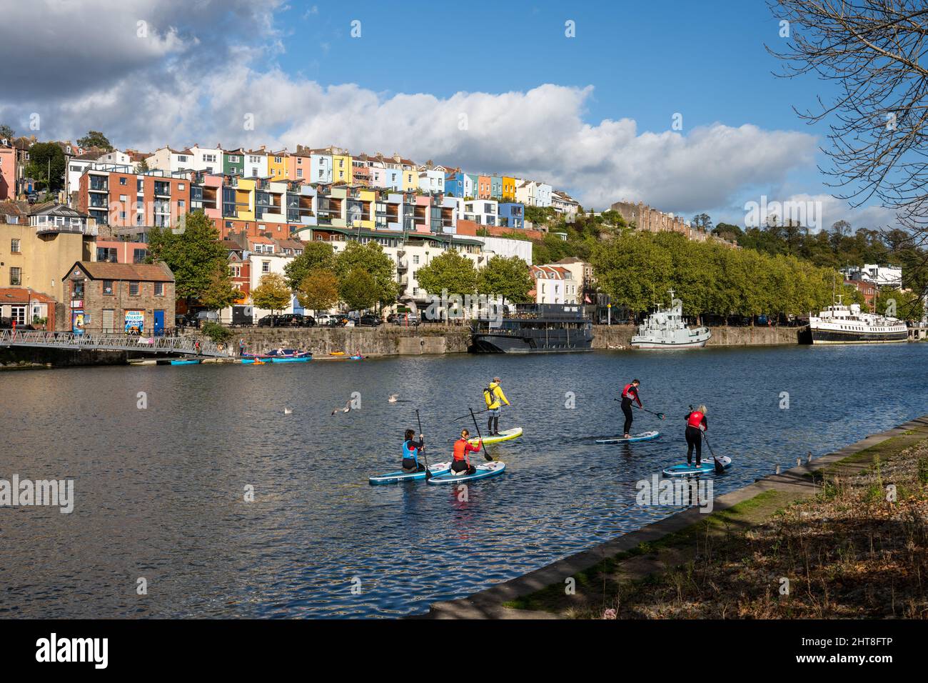 Un gruppo di pedalatori attraversa il porto galleggiante di Bristol, con le case di Clifton vale alle spalle. Foto Stock