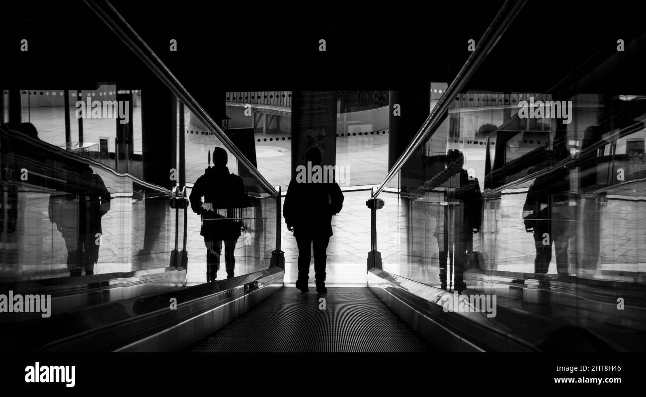 un uomo in piedi su una scala mobile in una biblioteca della città Foto Stock