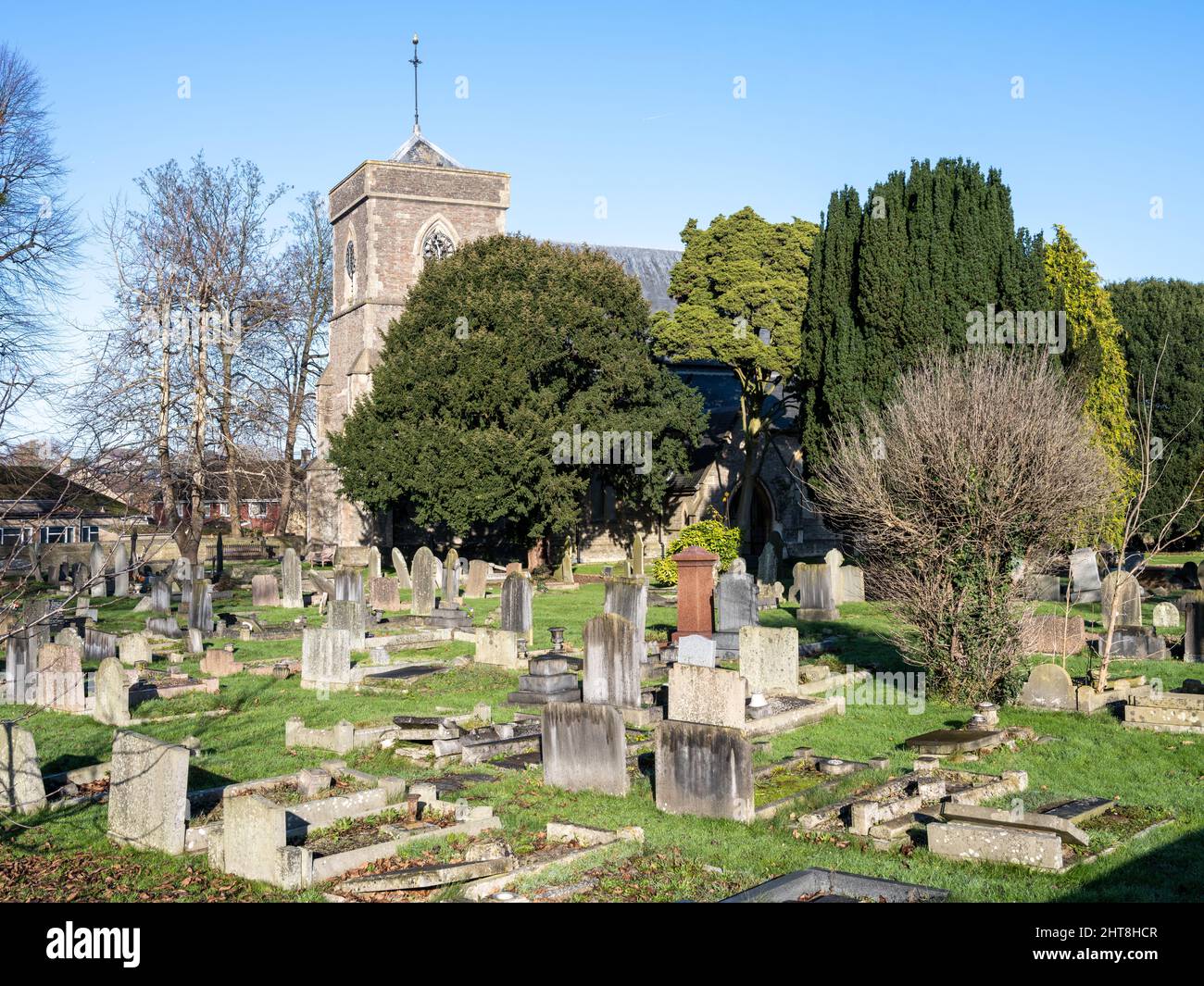 Il sole brilla sulla chiesa di San Salvatore e gli alberi di tasso e le lapidi nel cimitero di Coalpit Heath nel Gloucestershire del sud. Foto Stock