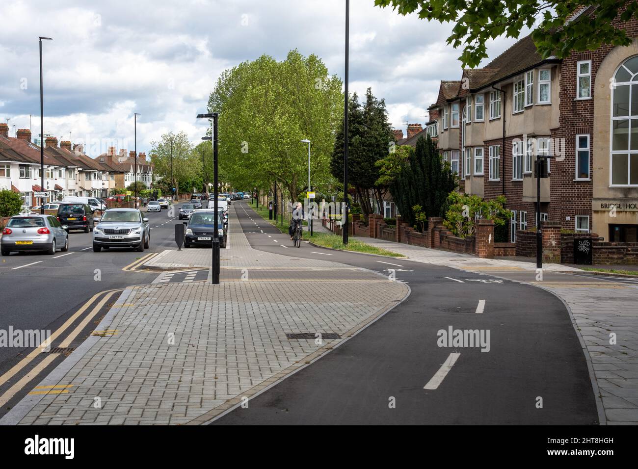 Un ciclista corre su una pista ciclabile protetta accanto ad una strada nella periferia ovest di Londra. Foto Stock