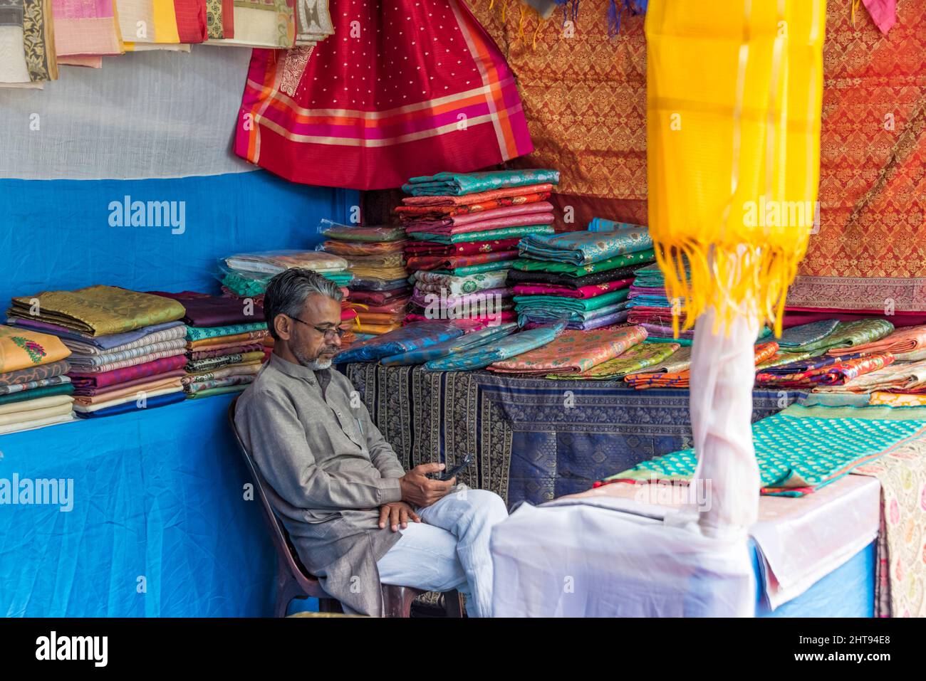 Uomo che guarda il telefono cellulare in un negozio che vende tessuto, Gangtok, Sikkim, India Foto Stock