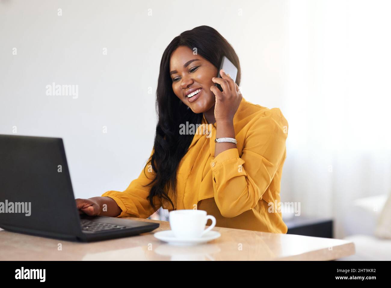 Lavorando come suo capo. Scatto di una giovane donna d'affari allegra che parla sul suo cellulare mentre lavora su un portatile a casa. Foto Stock