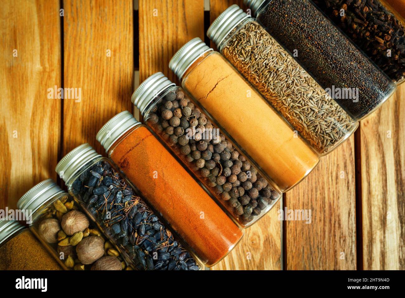 Diverse spezie multicolore in vasetti trasparenti giacciono su uno sfondo di legno. Foto Stock