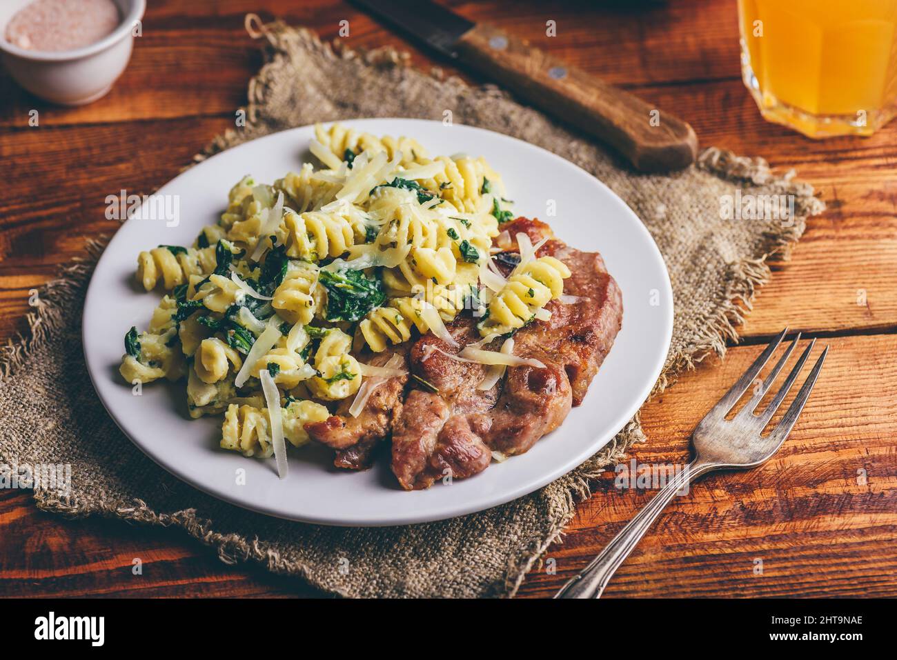 Bistecca di maiale con spinaci cremosi di pasta guarnita con grattugiata Parmigiano su piatto bianco Foto Stock