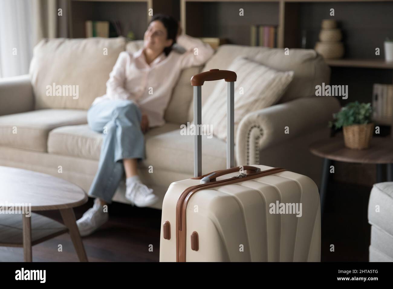 Concentrati sulla valigia beige con donna sfocata e rilassata sullo sfondo. Foto Stock