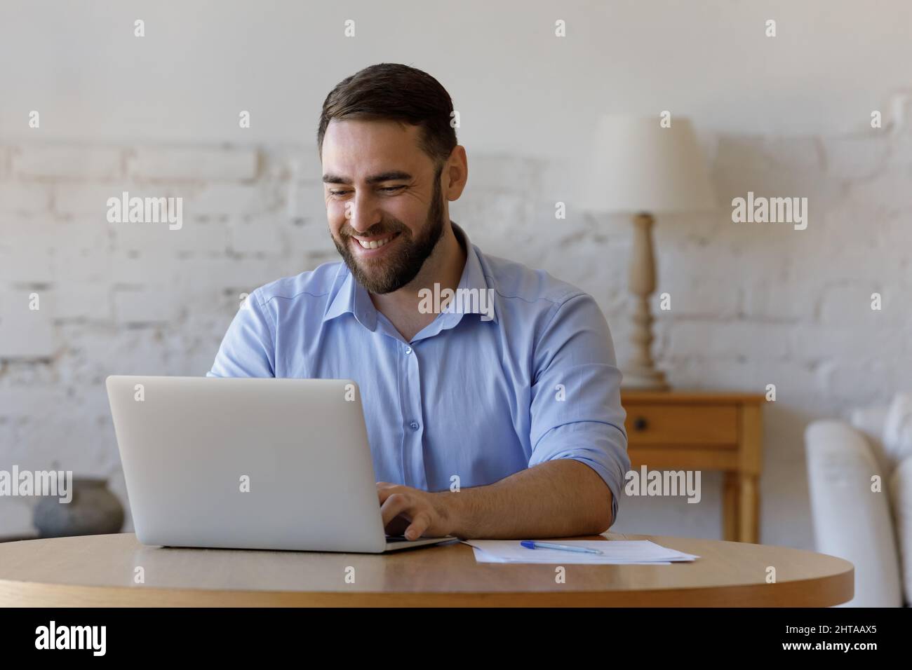 Il giovane e bell'uomo freelance si siede al tavolo usando un laptop Foto Stock