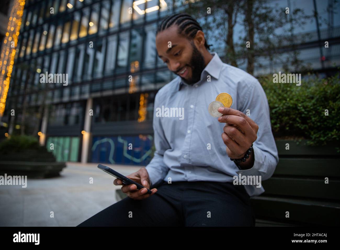 Un commerciante di criptovaluta è felice con i risultati dei suoi investimenti, ha il suo smartphone, un Bitcoin e moneta etereo in mano Foto Stock