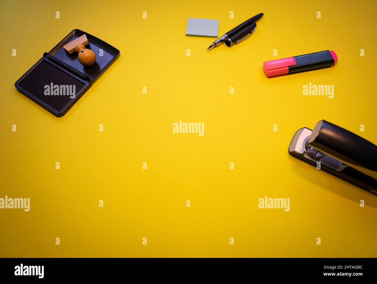 Vista dall'alto di un timbro di legno con inchiostro, graffatrice metallica, note adesive e marcatori isolati su sfondo giallo Foto Stock