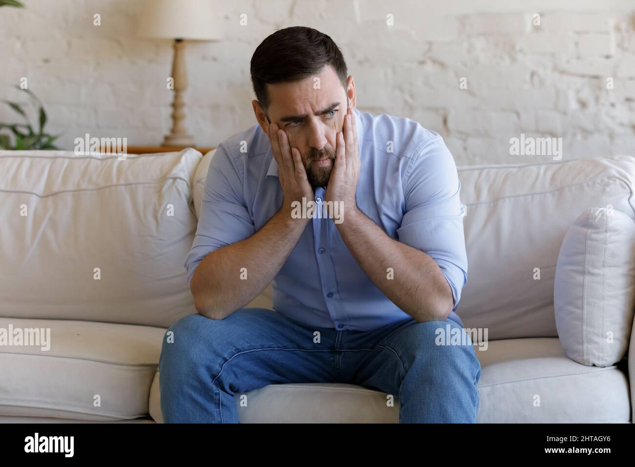 L'uomo seduto sul divano sembra depresso, pensando ai problemi Foto Stock