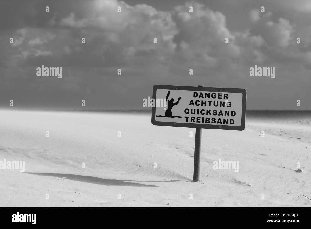 Un'immagine in scala di grigi del segnale di avvertimento sulla spiaggia in una giornata di sole Foto Stock