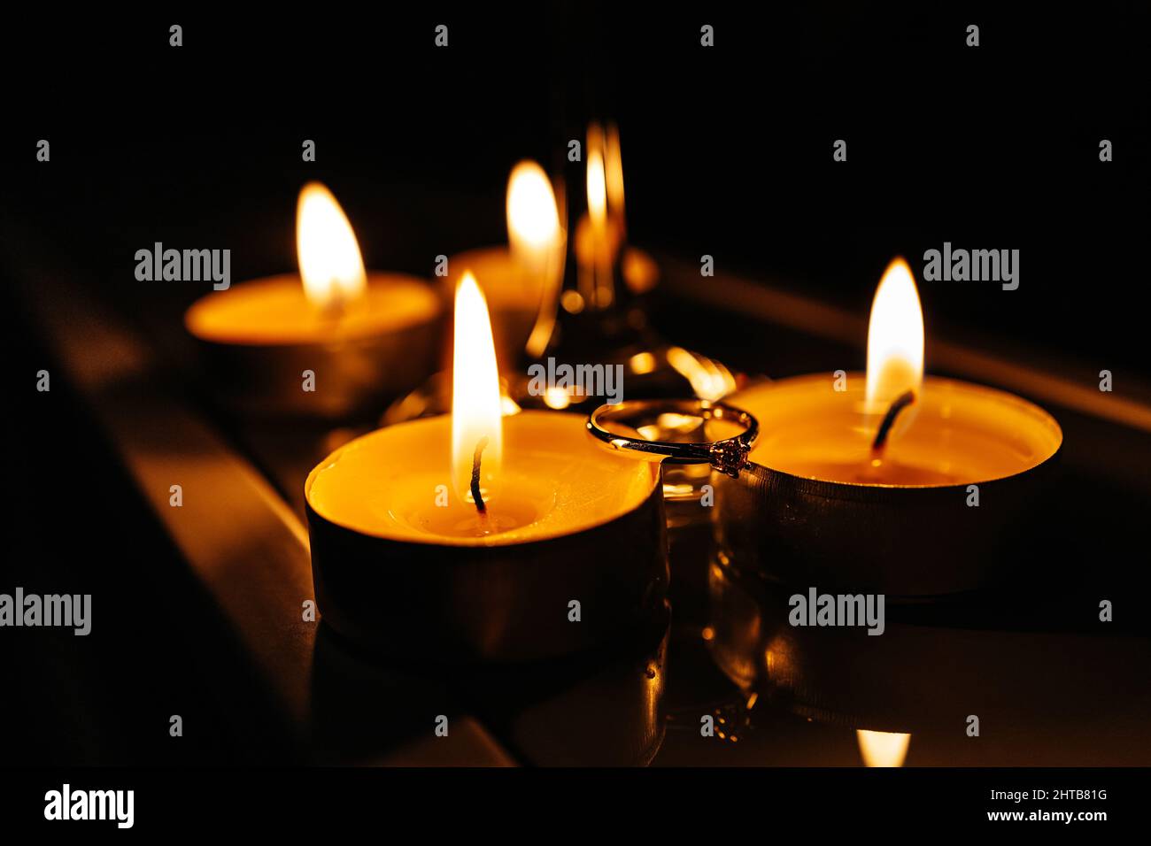 Primo piano di un anello di impegno tra le candele che bruciano Foto Stock