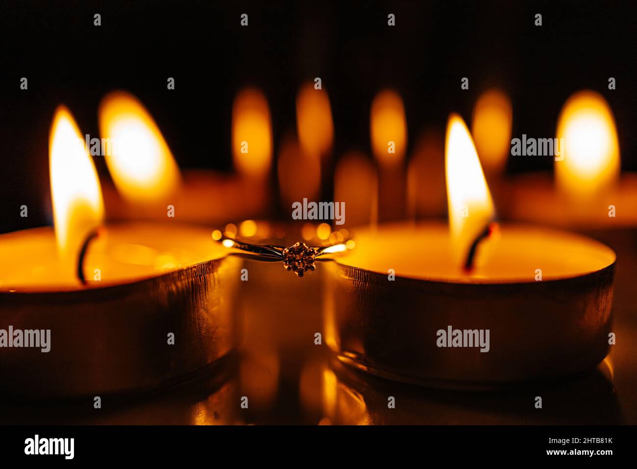 Primo piano di un anello di impegno tra le candele che bruciano Foto Stock