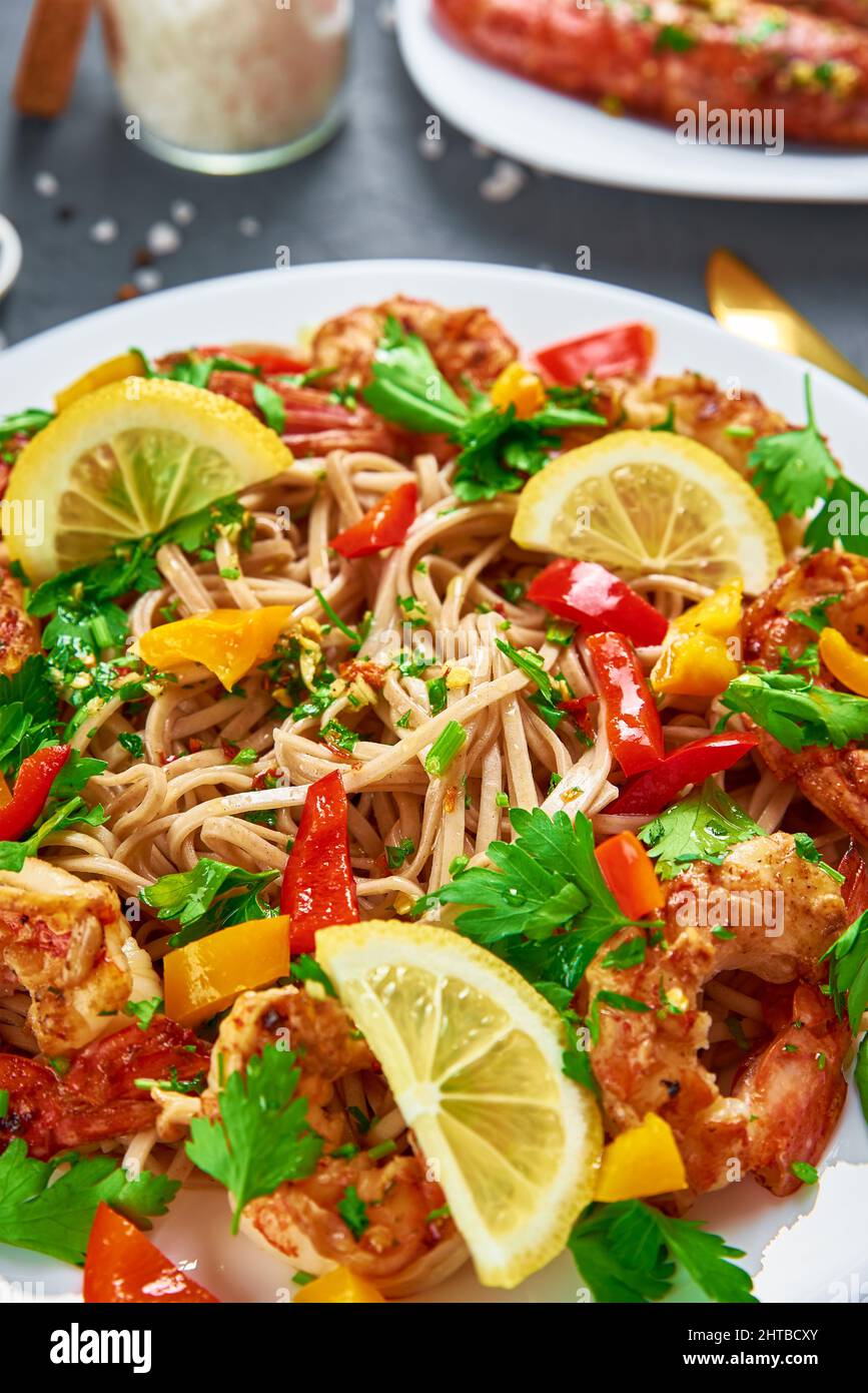 Friggete la noodle con gamberi, limone e prezzemolo fresco sul piatto bianco, soba con gamberi, cucina asiatica, vista dall'alto Foto Stock