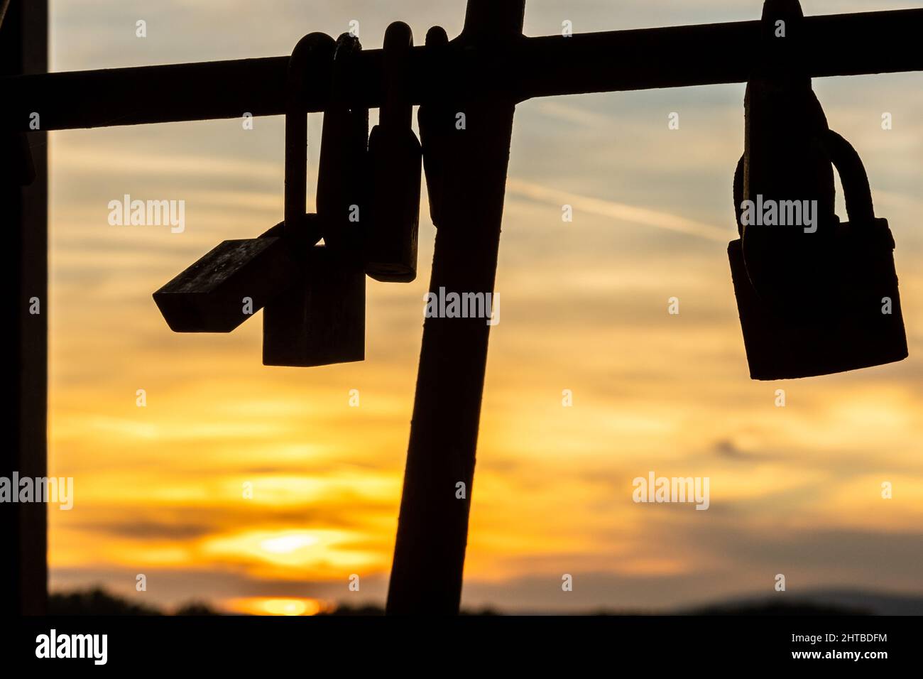 Silhouette di alcune serrature appese su fili metallici sullo sfondo di un tramonto. Foto Stock