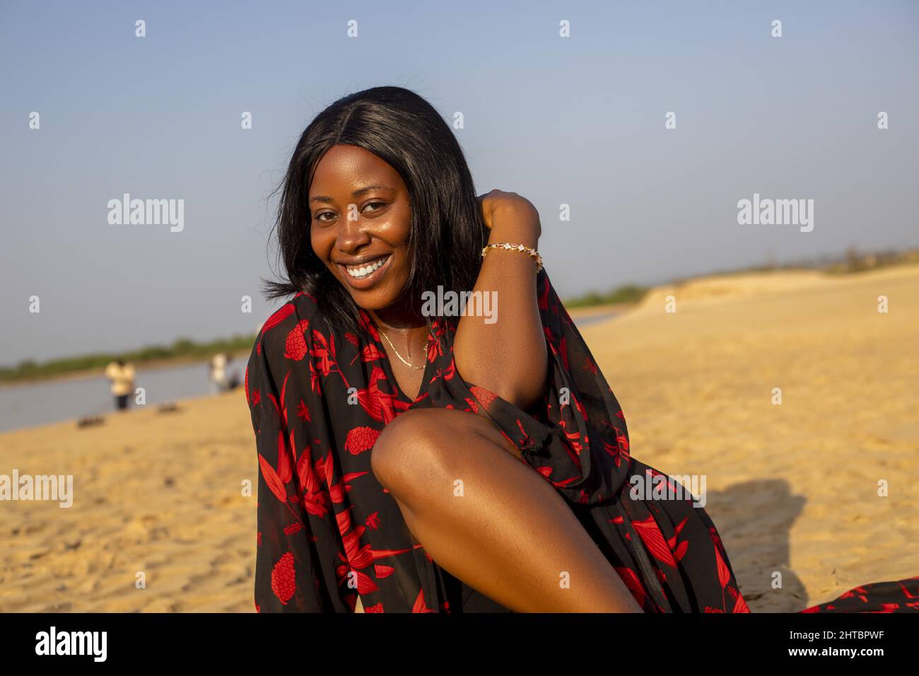 Una giovane donna africana attraente sorridente e posata sulla spiaggia Foto Stock