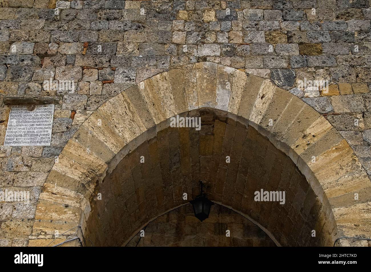 L'iscrizione latina accanto ad un arco porta riporta la fondazione di Monteriggioni da parte di Siena nel 1213 come fortezza collinare costruita per resistere ai ripetuti attacchi di Firenze nelle inesorabili guerre tra le due più importanti città medievali della Toscana, Italia. Foto Stock