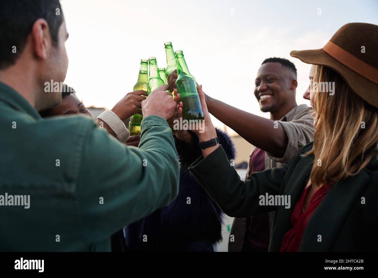 Gruppo multiculturale di giovani adulti che fanno un brindisi e ridono con bevande sul balcone di una terrazza sul tetto della città. Foto Stock