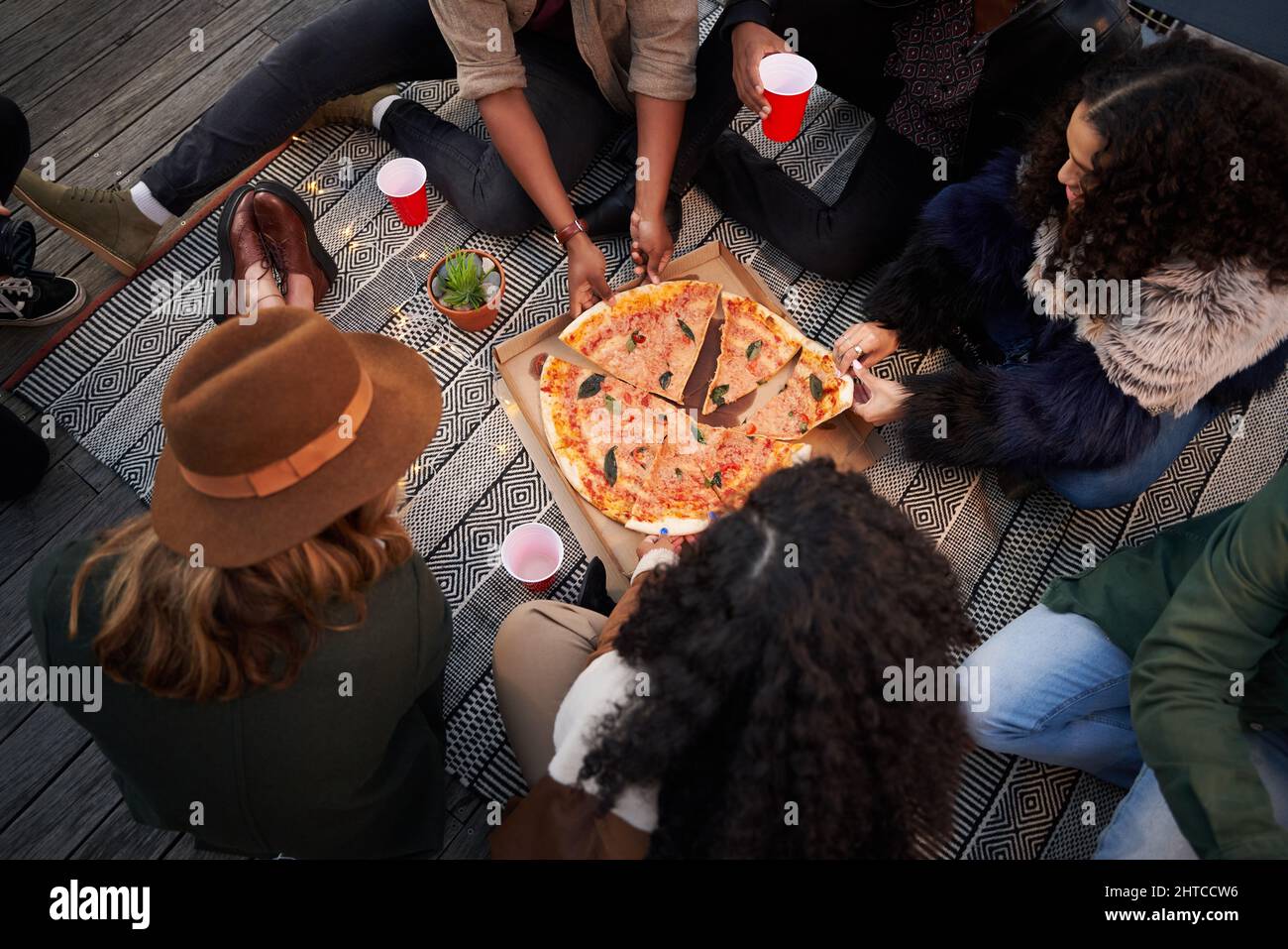 Gruppo di amici diversi che si affettano pezzi di pizza da mangiare mentre si siede sulla terrazza sul tetto della città Foto Stock