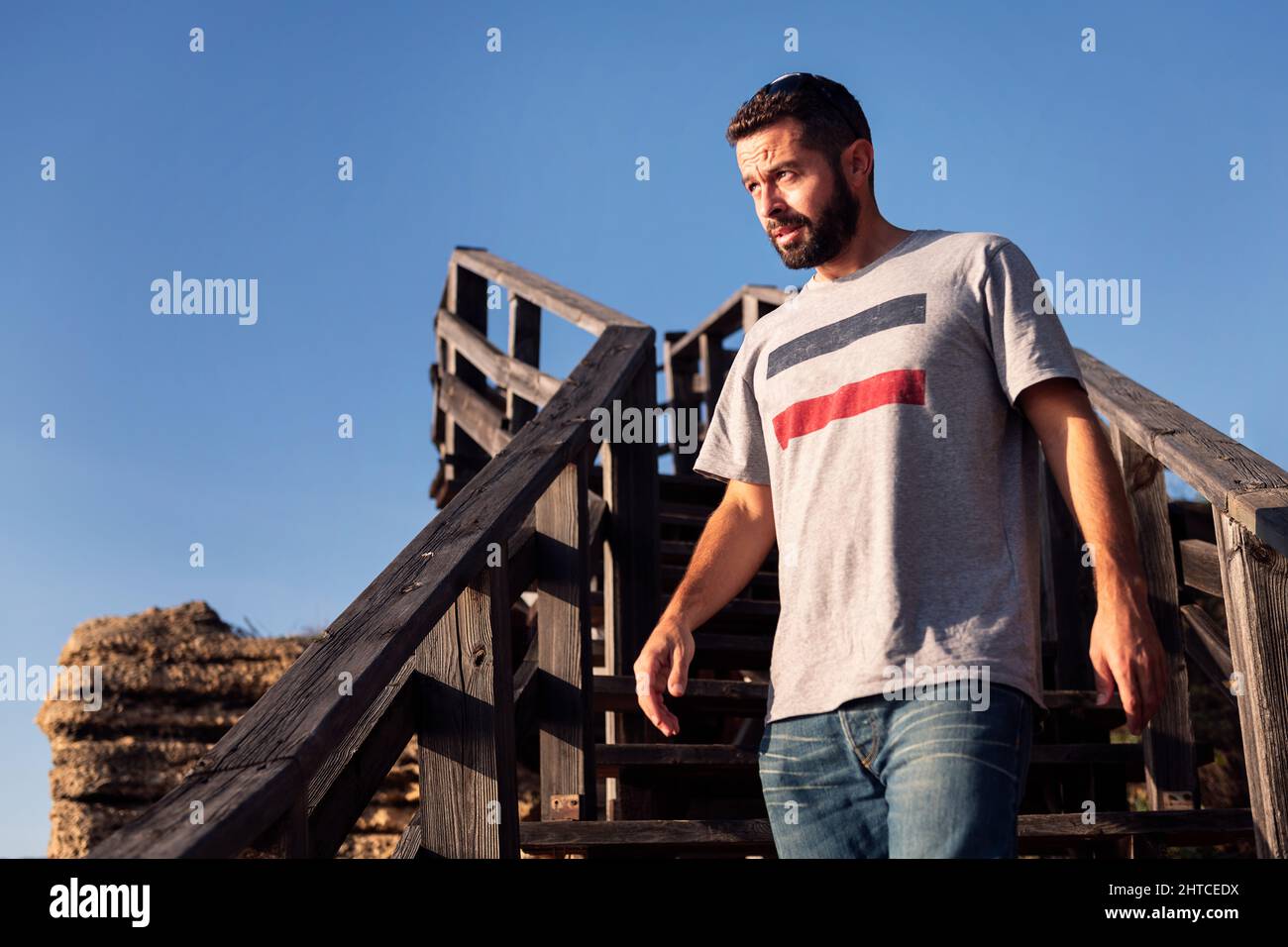 bel giovane uomo che cammina lungo una scala di legno con il cielo blu sullo sfondo, concetto di tempo libero e relax, spazio copia per il testo Foto Stock