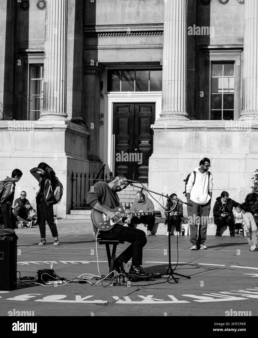 Scala di grigi verticale di un busker che gioca a "Wicked Game" di Chris Isaak al Trafalgar Square, Londra Foto Stock