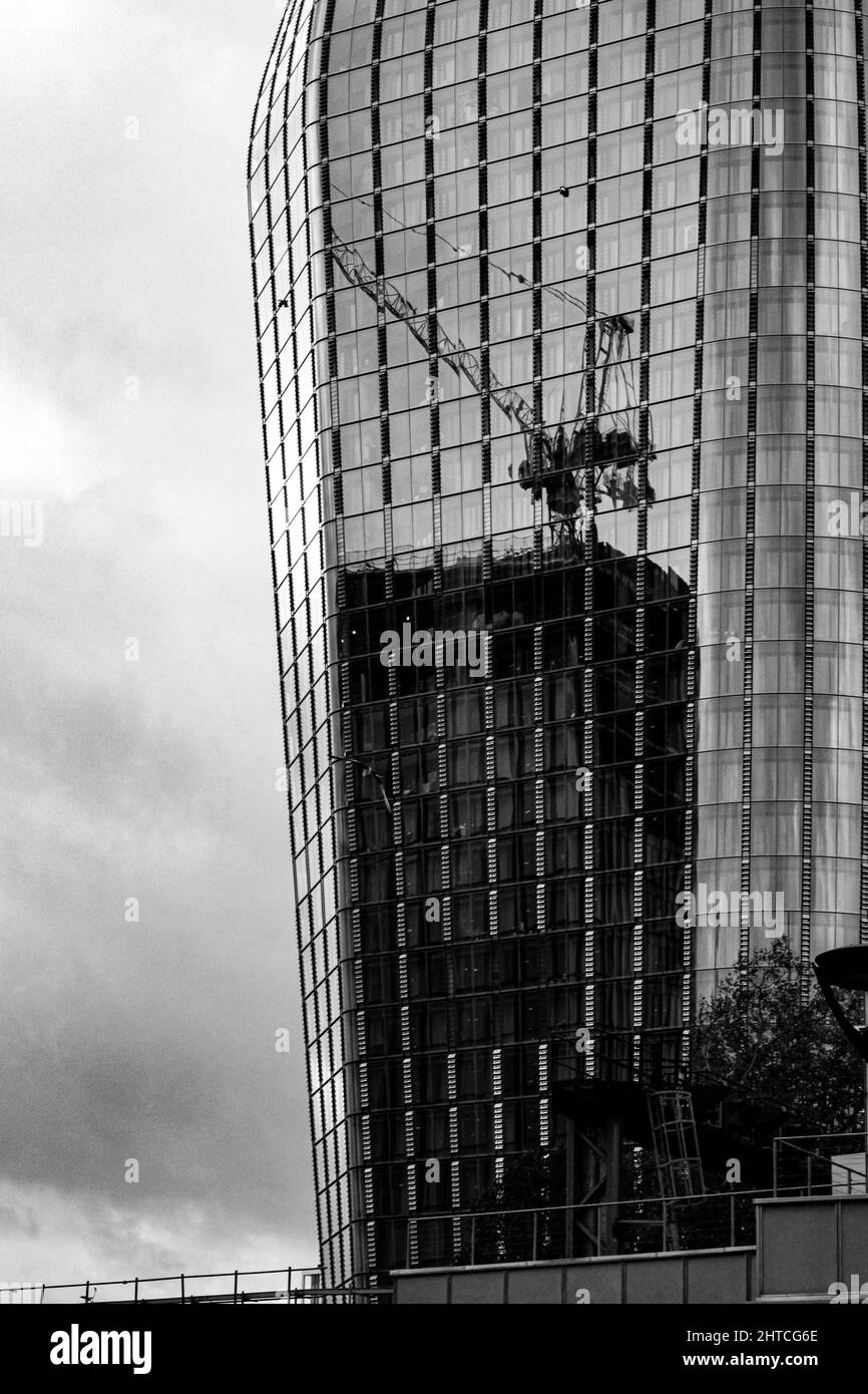 Scatto verticale in scala di grigi di un grattacielo a Londra e di una gru da cantiere davanti ad esso, il Regno Unito Foto Stock