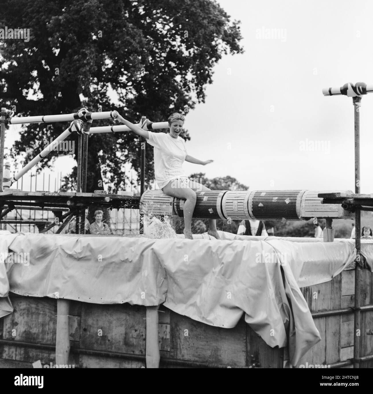 Laing Sports Ground, Rowley Lane, Elstree, Barnet, Londra, 11/06/1988. Una donna seduta a cavalcare un fascio rotante di bilanciamento su un serbatoio d'acqua, mentre le vengono lanciate spugne bagnate, parte del concorso "IT's a Knockout" al Family Day del Laing's Sports Ground del 1988. Le attrazioni del Family Day di quell'anno sono incluse: Una sfilata di auto d'epoca, giri in elicottero, sbattimento dei piatti, bancarelle, una competizione in stile "IT's a Knockout" e tornei di tennis e calcetto. L'evento è stato aperto da John Conteh, ex campione mondiale di pesi leggeri e si è concluso con un barbecue e una discoteca. Questa foto Foto Stock