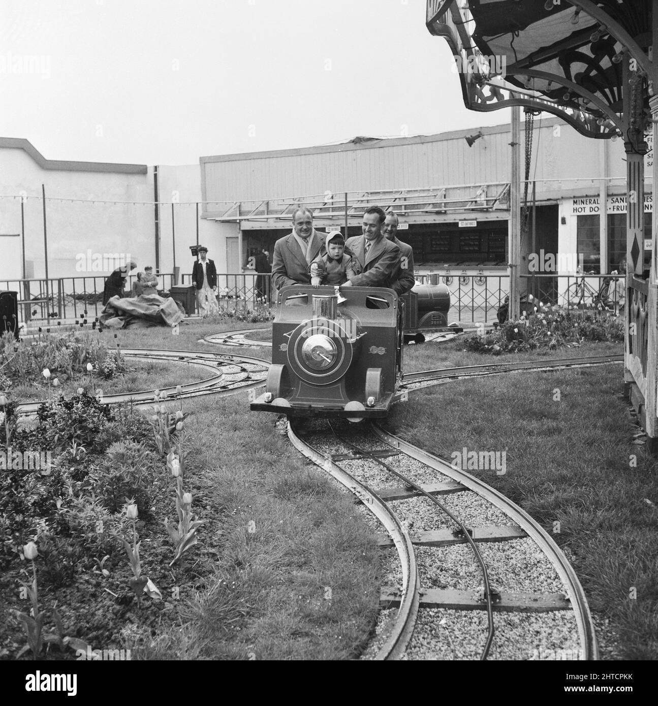 Skegness, East Lindsey, Lincolnshire, 22/05/1954. Tre uomini accompagnano un bambino che viaggia su un motore ferroviario in miniatura durante un viaggio del personale di Laing a Skegness. Nel 1947, dopo una pausa di sette anni, Laing aveva risuscitato le loro "uscite di zona" per il personale e le loro famiglie, con viaggi in maggio e giugno. Nel 1954 sono state previste sette uscite per cinque settimane a maggio e giugno. Questo viaggio a Skegness è stato per i dipendenti e le loro famiglie delle Midlands e del South Yorkshire. Foto Stock