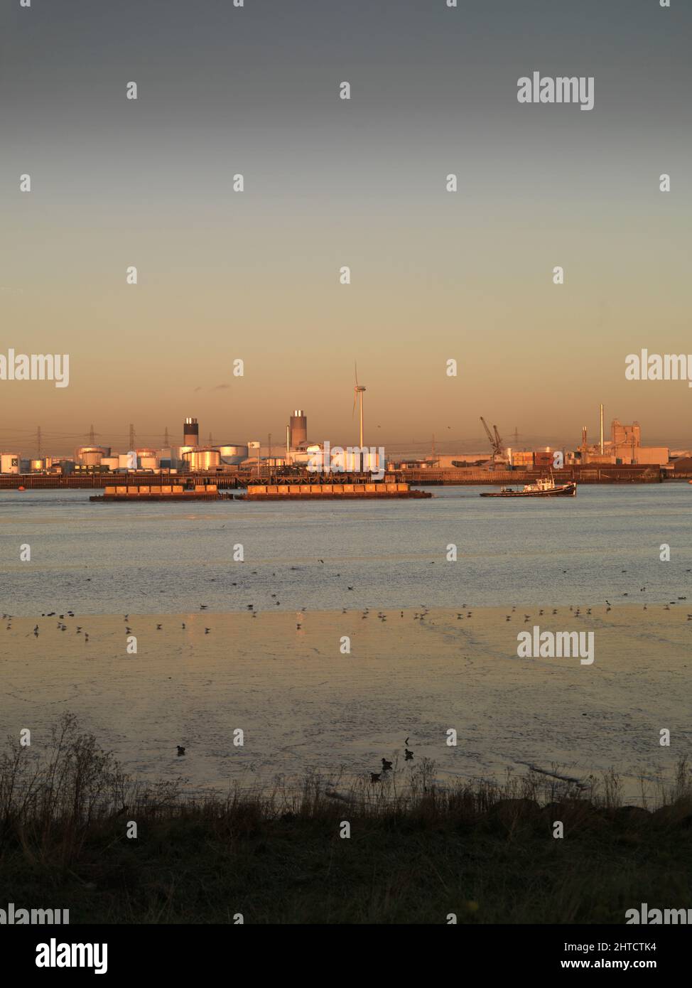 Thamesmead, Bexley, Londra, 2006. Vista generale guardando verso nord-est attraverso il Tamigi da Thamesmead verso Dagenham al tramonto, con un rimorchiatore che viaggia a valle, tirando due chiatte caricate di contenitori di spedizione. Foto Stock