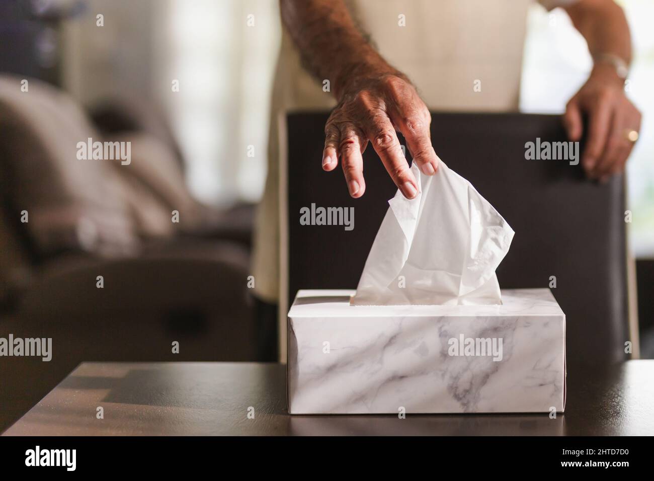 Mano uomo anziano che raccoglie carta di tessuto dalla scatola di tessuto sul tavolo da pranzo. Foto Stock