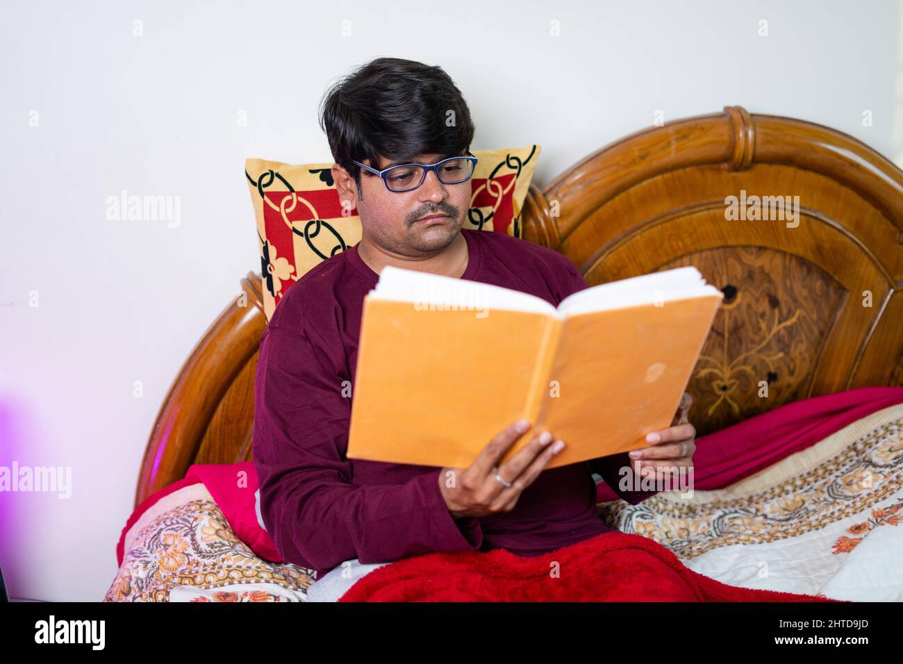 giovane uomo con occhiali leggere libro prima di dormire in camera da letto - concetto di hobby, benessere e routine notturna Foto Stock