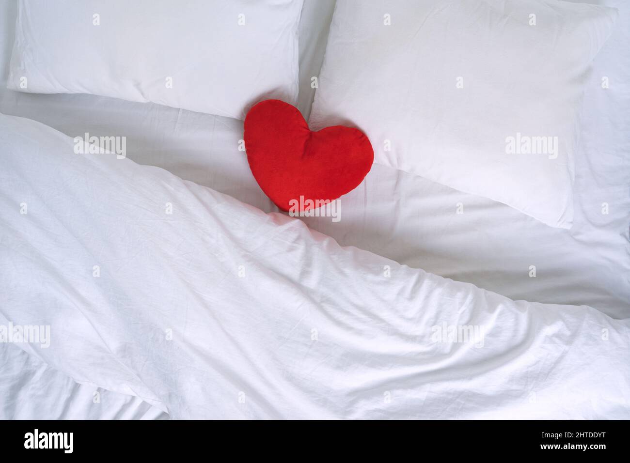 Vista dall'alto del letto bianco con cuscini e giocattolo per leggere il cuore Foto Stock
