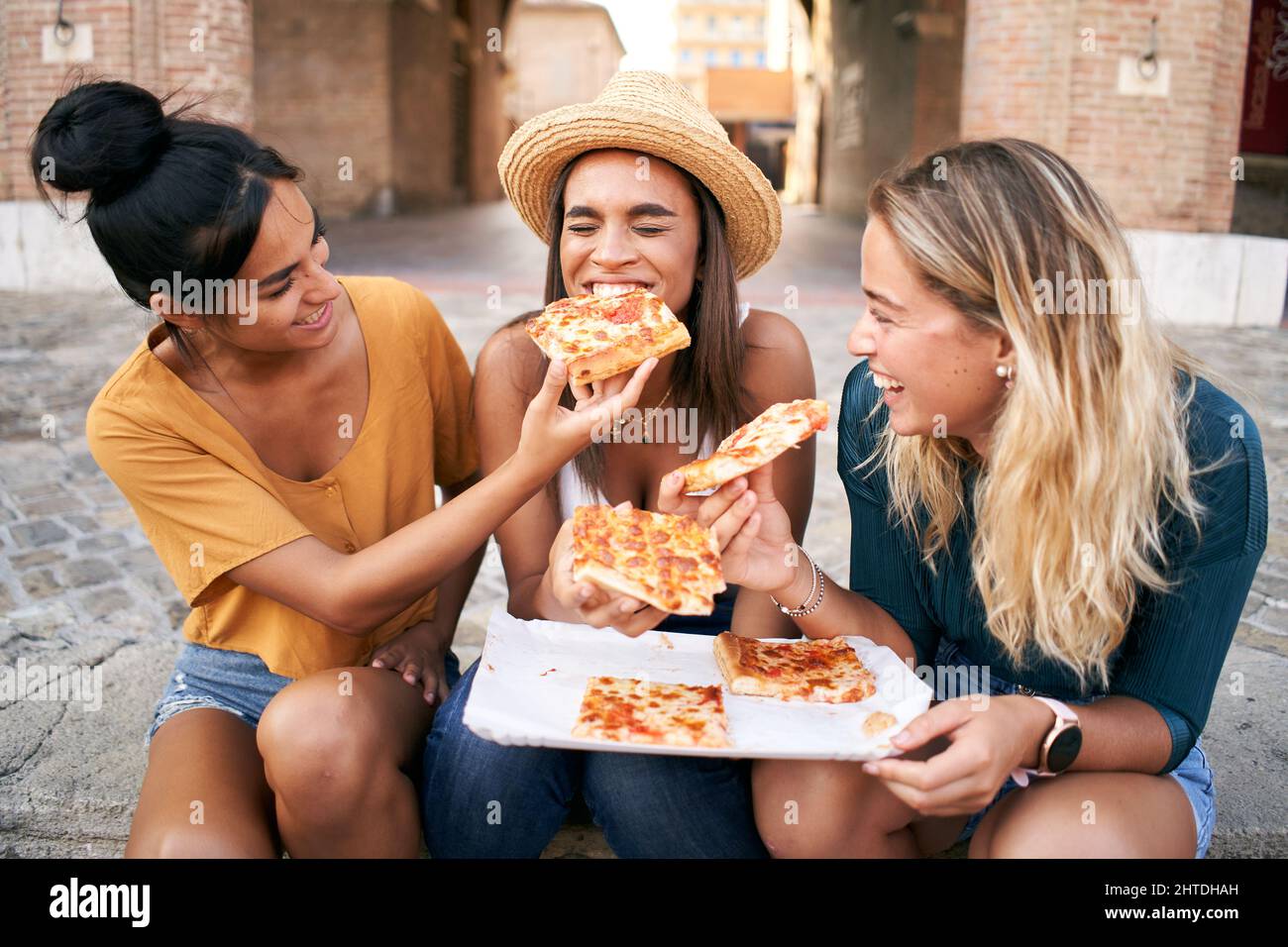 Buone amiche che mangiano pizza Street food in città. Gruppo turistico femminile di tre donne che si divertono. Una ragazza nutre l'altra. Stile di vita e. Foto Stock