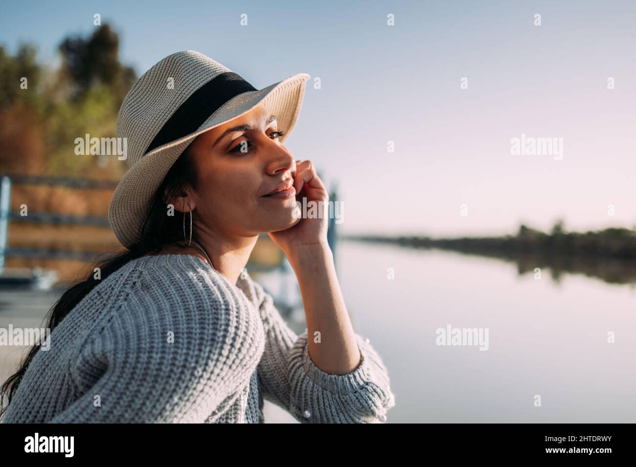 Primo piano di donna latina con cappello rilassante sul bordo di un molo vicino ad un lago Foto Stock