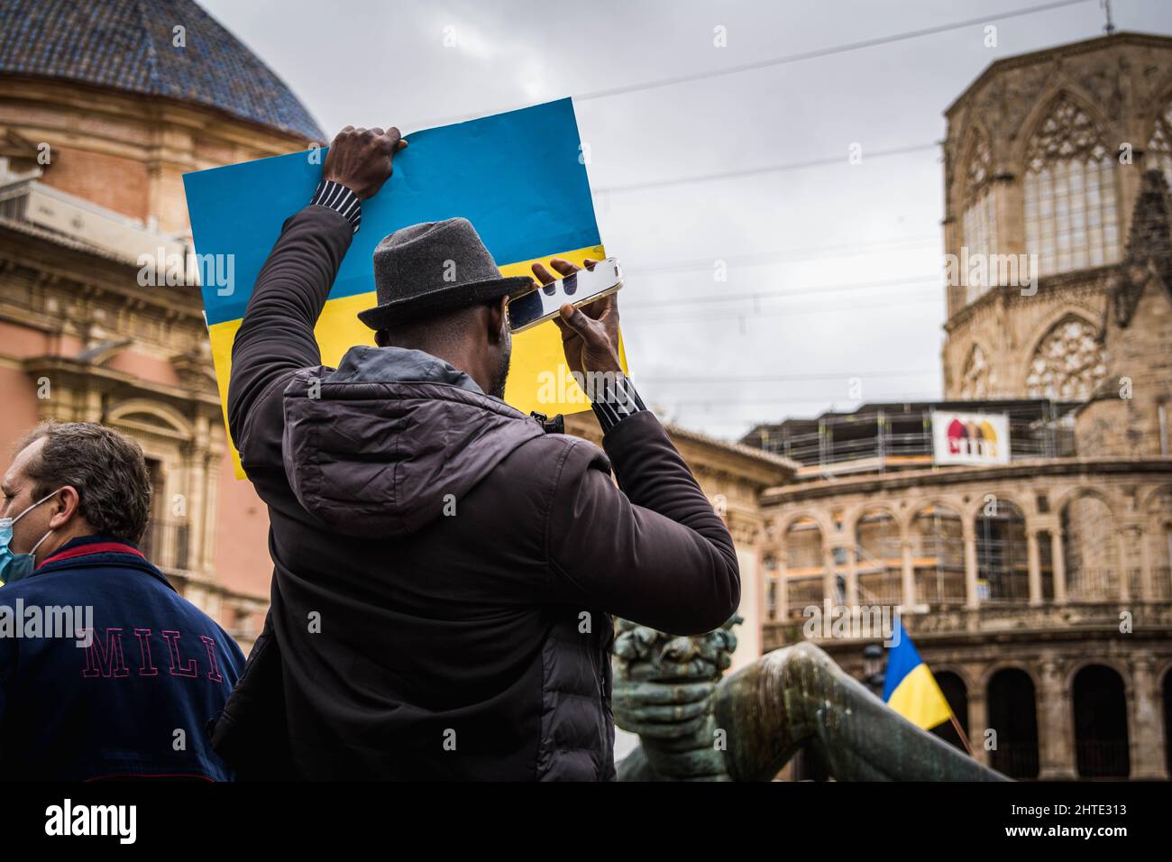 Black Man con cappello ascoltare l'audio sul suo cellulare mentre tiene una bandiera Ucraina in una protesta Foto Stock